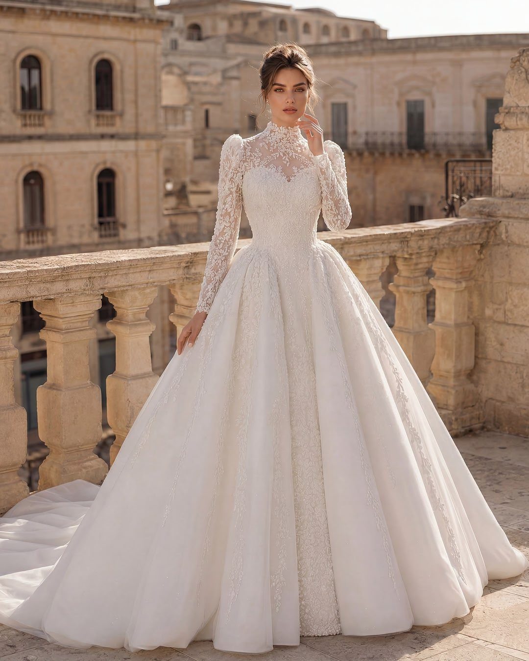 Woman in a white lace long-sleeved ballgown wedding dress on a stone balcony.