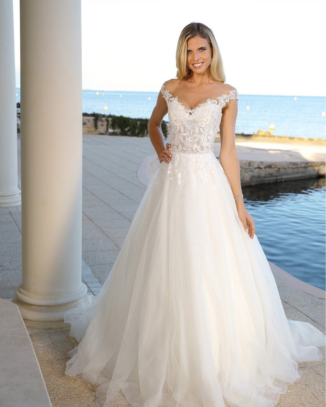 Woman in a white A-line wedding dress with lace bodice standing by the sea.