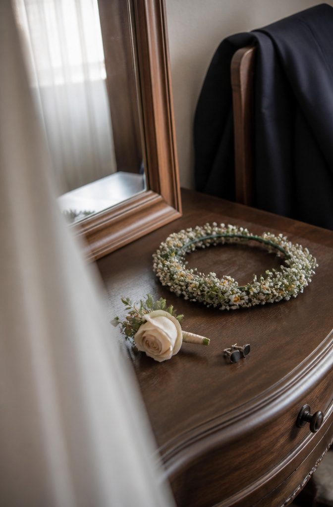 Pale rose boutonniere beside a flower crown with baby’s breath and daisies
