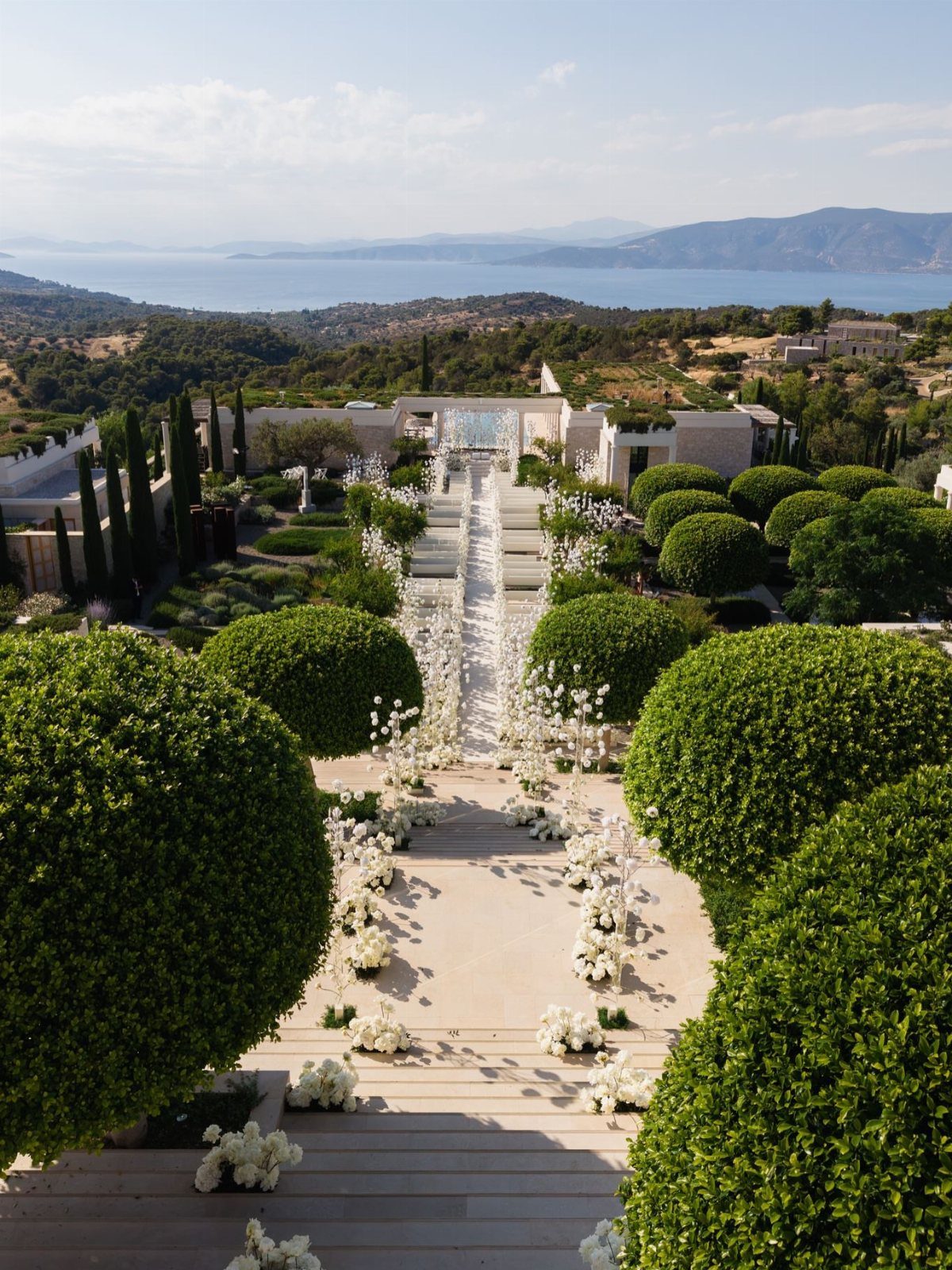 Luxury wedding venue with white floral aisle and manicured shrubs overlooking the Greek coast.