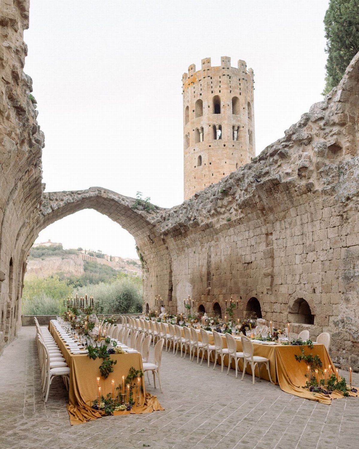 Wedding banquet table with yellow linens set among ancient stone ruins and a tower.