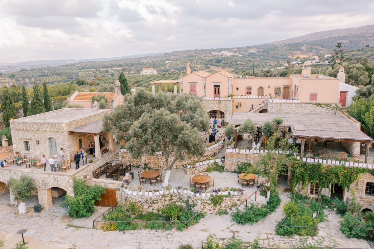 Stone estate with outdoor dining and olive trees overlooking a Greek countryside landscape.