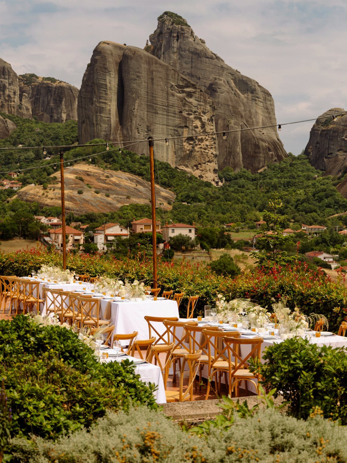 Outdoor wedding reception tables with white linens set against towering Greek rock formations.