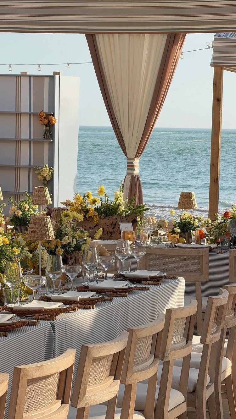 Beach wedding table setting with yellow flowers and white curtains overlooking the blue ocean