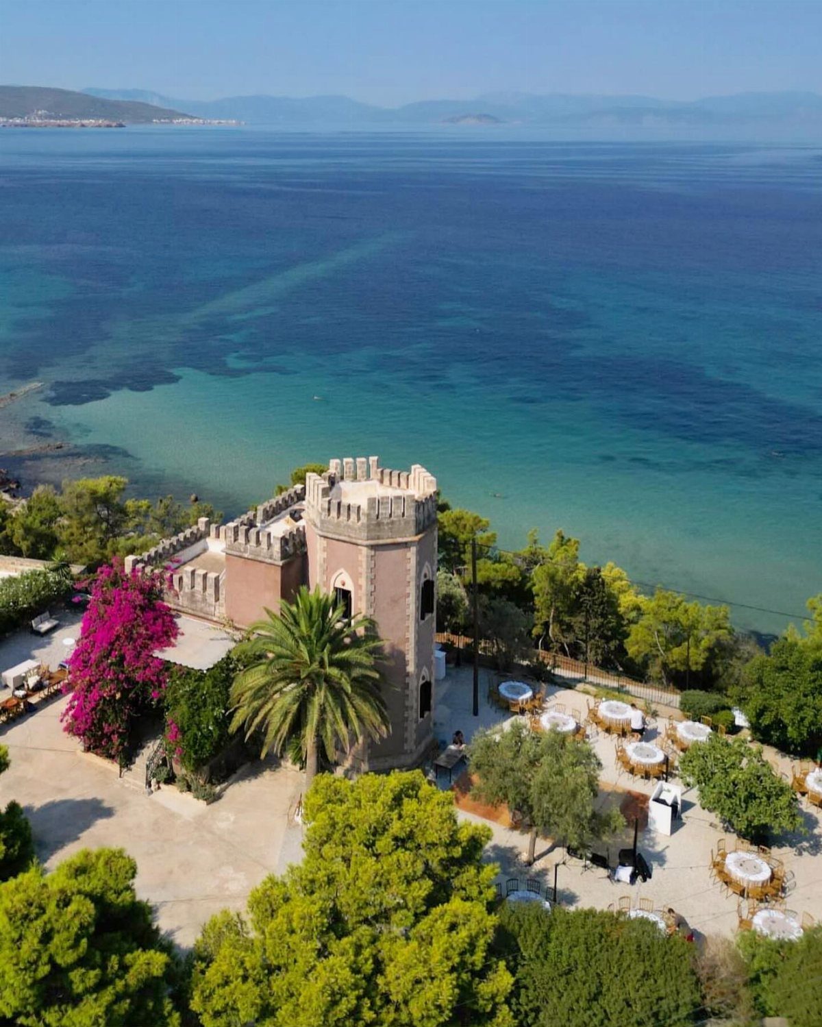Stone castle villa with outdoor dining area overlooking a turquoise Greek sea
