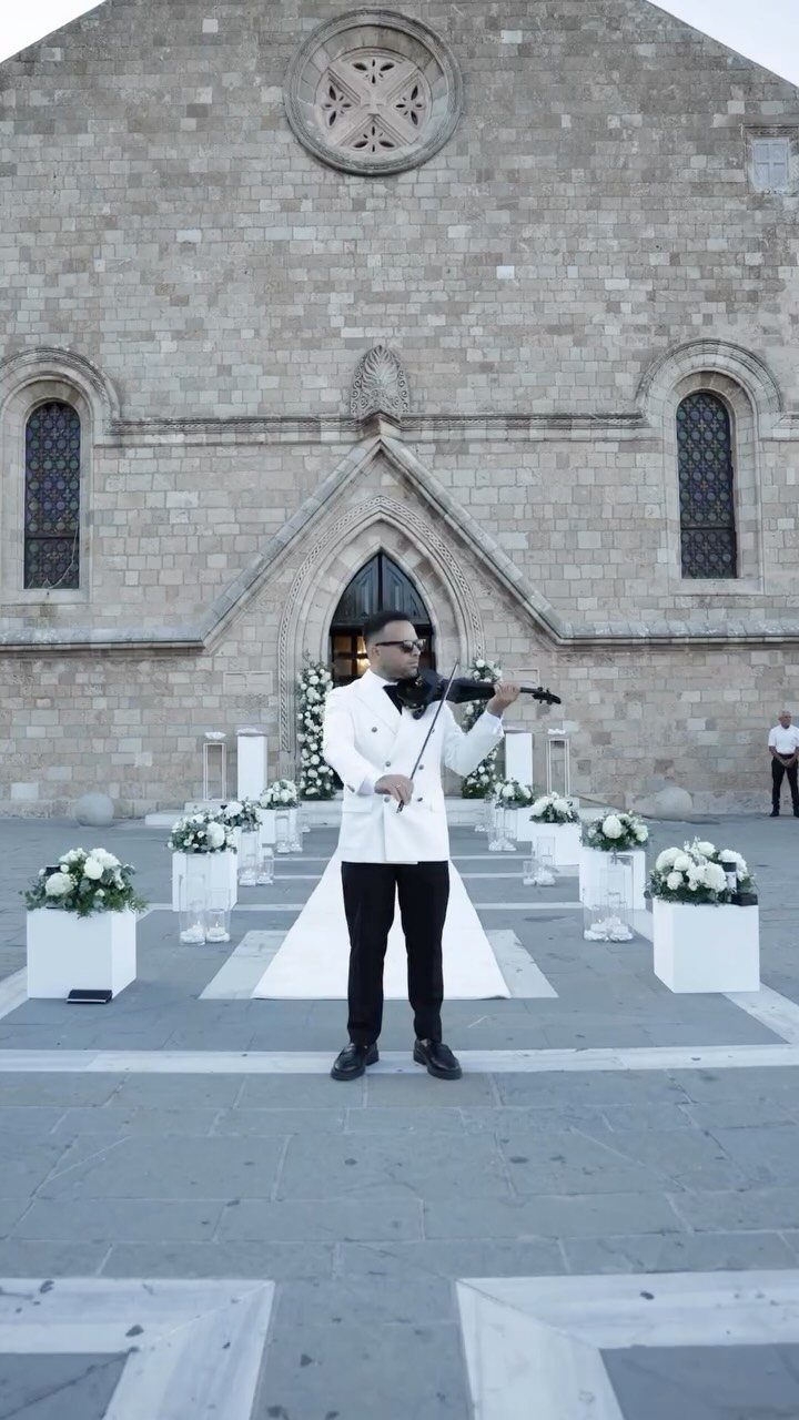 Violinist playing in front of a historic stone building with white wedding floral arrangements