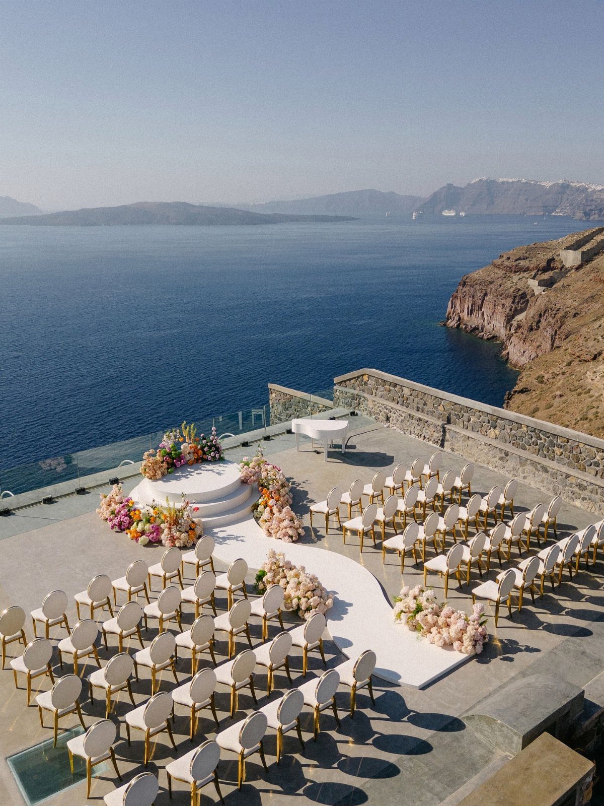 Wedding ceremony setup on a cliffside terrace overlooking the blue Aegean sea and caldera.