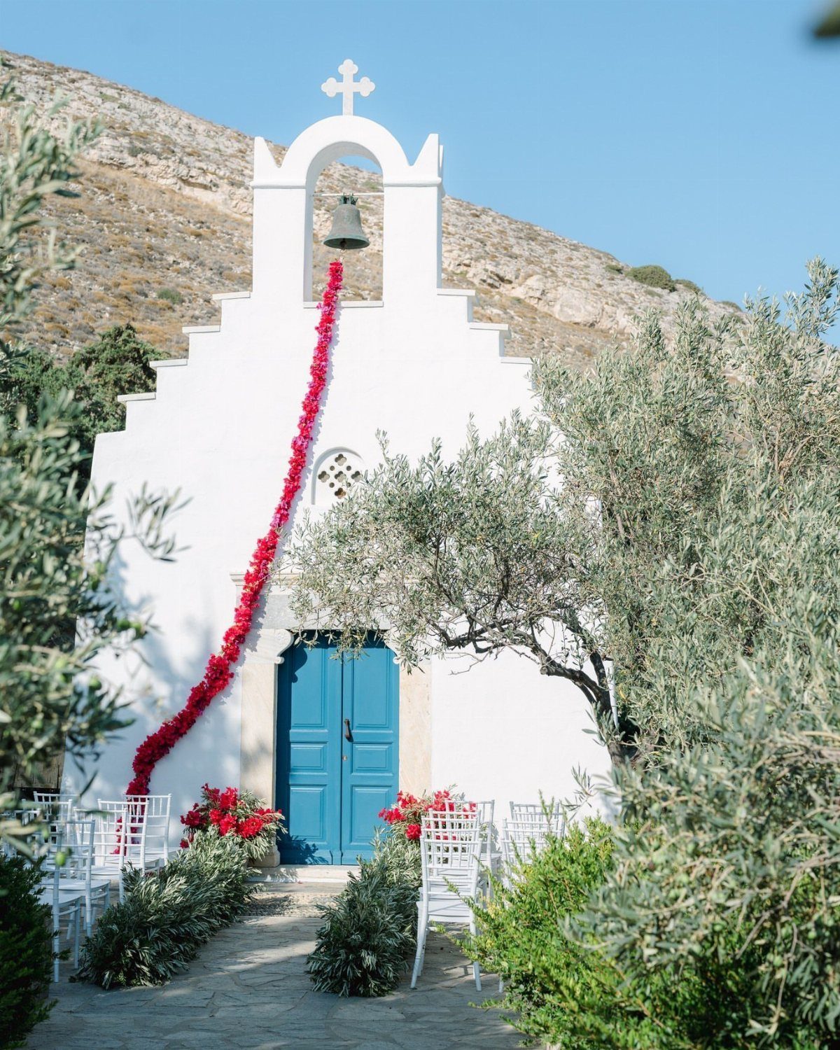 White Greek chapel with blue door and red flower garland for a wedding ceremony.