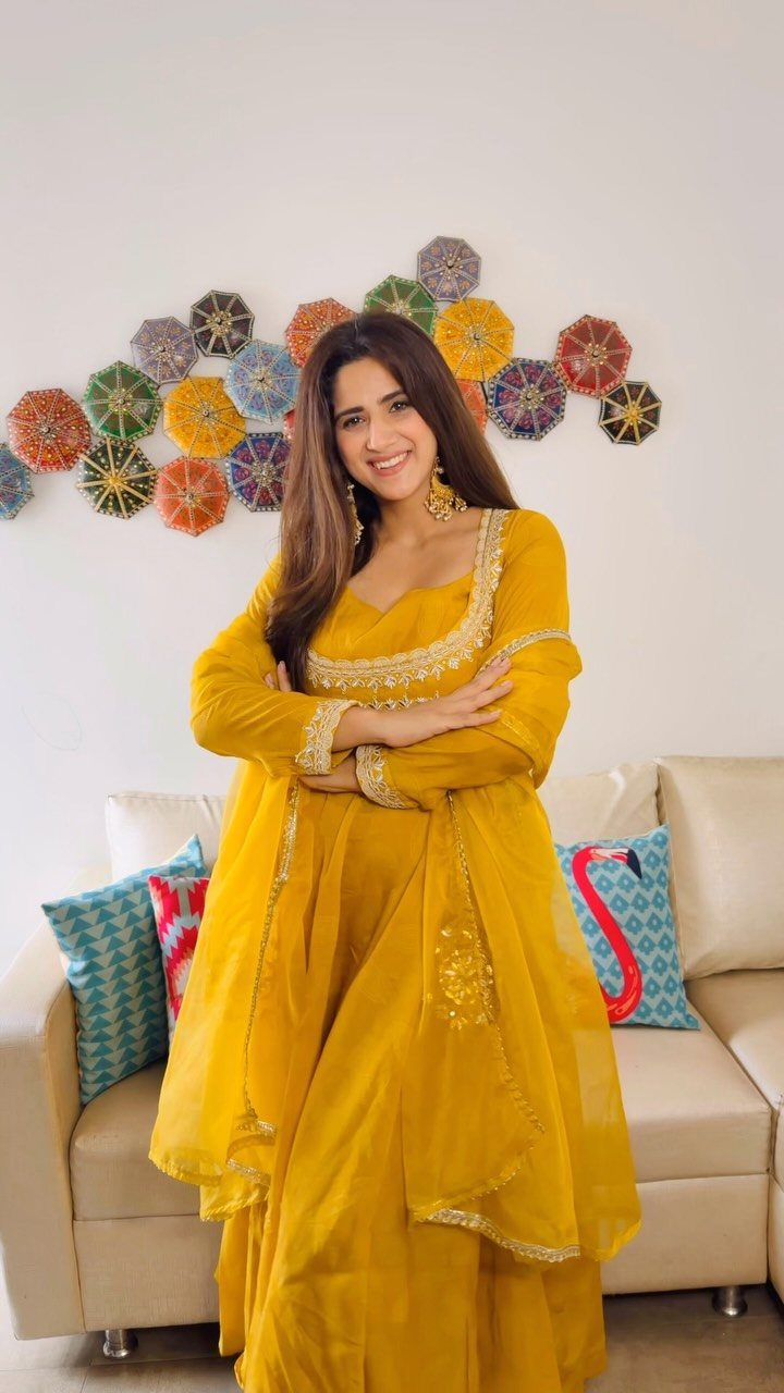 Woman in a yellow Anarkali suit set with gold embroidery posing indoors.