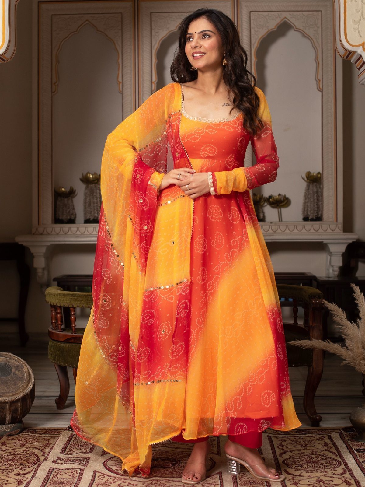 Woman wearing a yellow and orange bandhani print Anarkali suit with a matching dupatta.