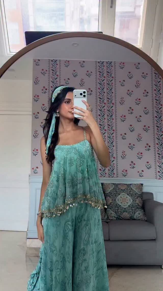 Woman in a light blue-green embroidered suit set taking a mirror selfie.