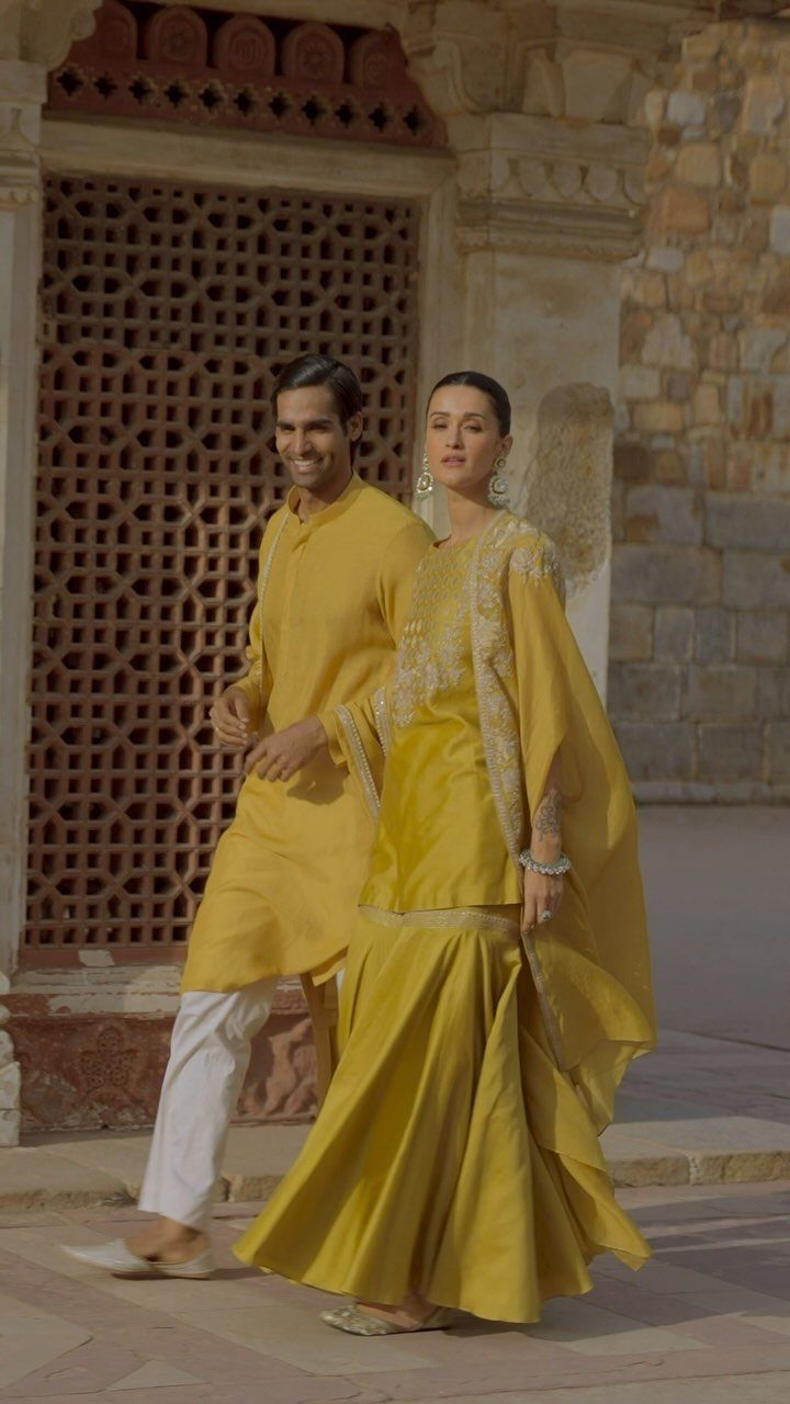 Woman in yellow embroidered cape kurta and skirt posing with man in yellow kurta