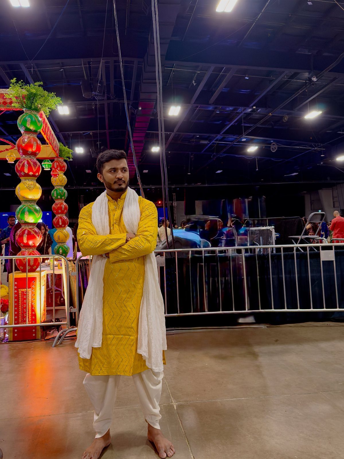 Man in yellow kurta and white dhoti pants standing in a decorated venue.