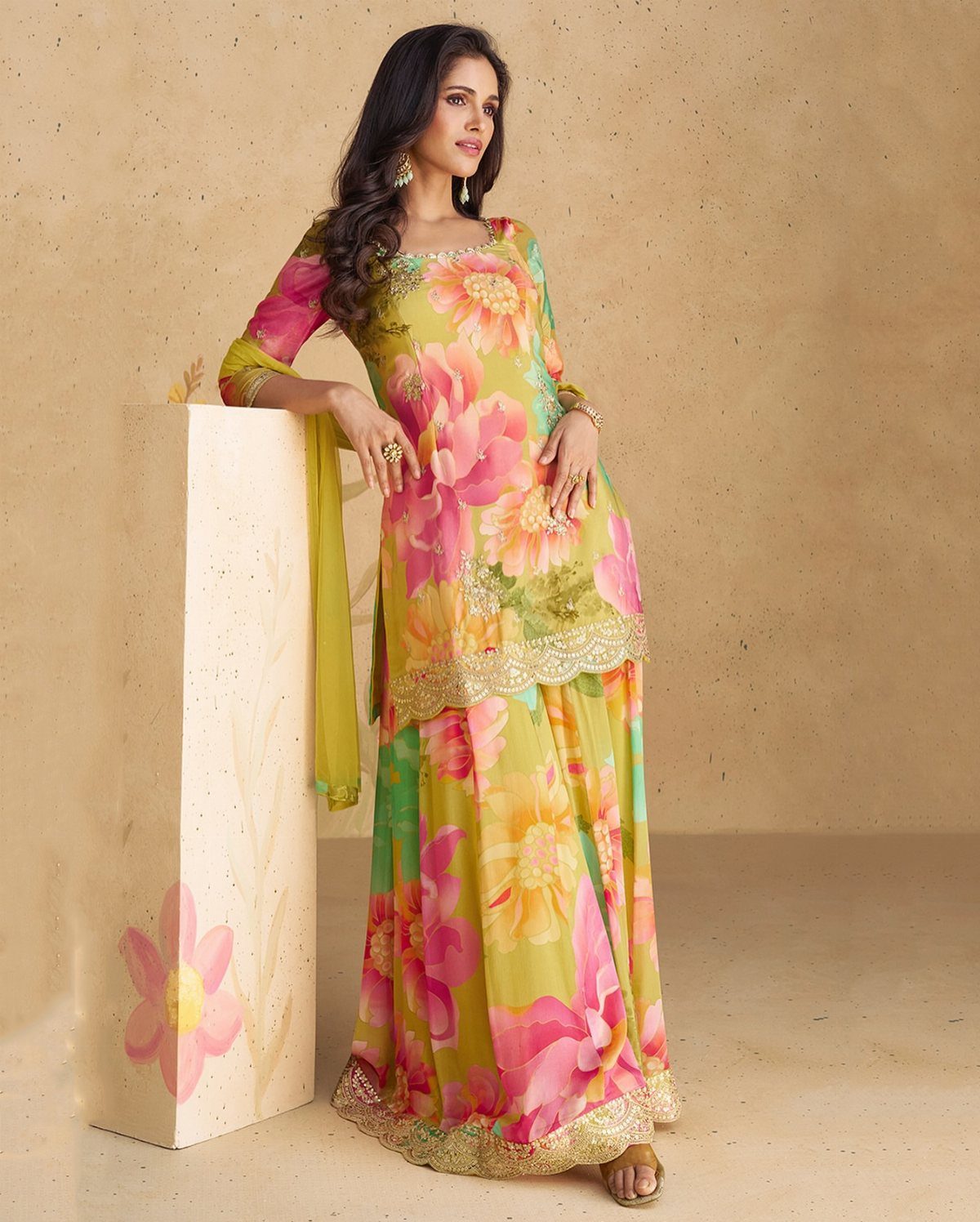Woman wearing a yellow and pink floral print salwar kameez with gold borders.