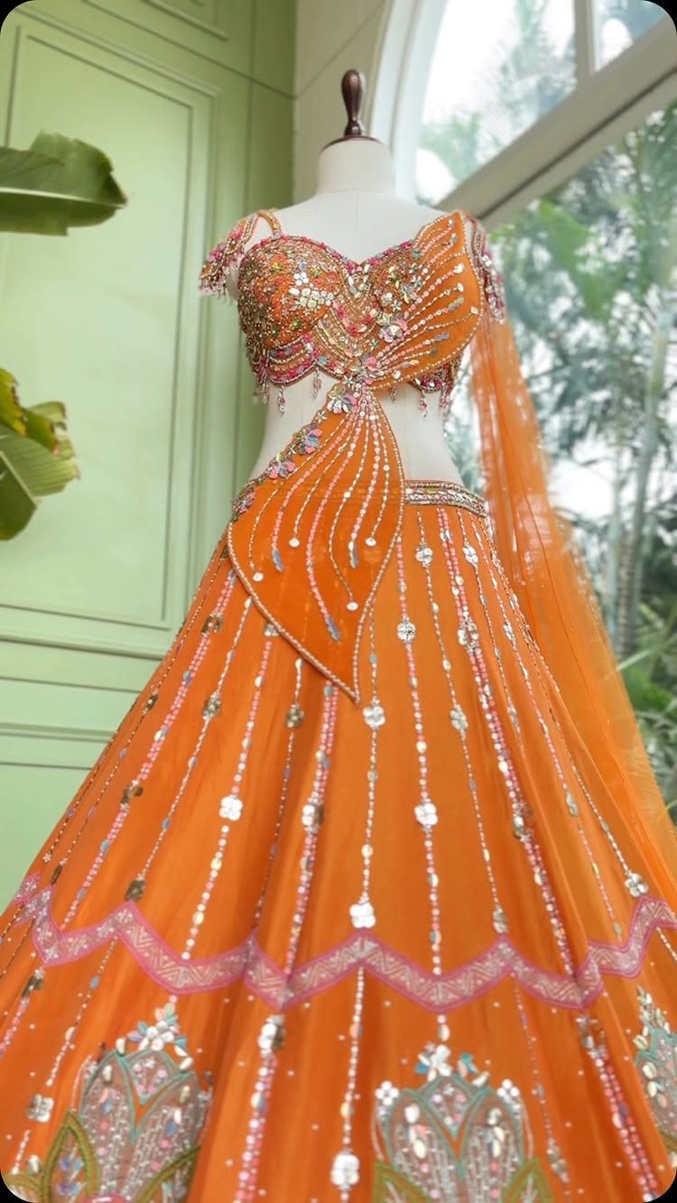 Orange lehenga choli with mirror work and sequins displayed on a white mannequin.
