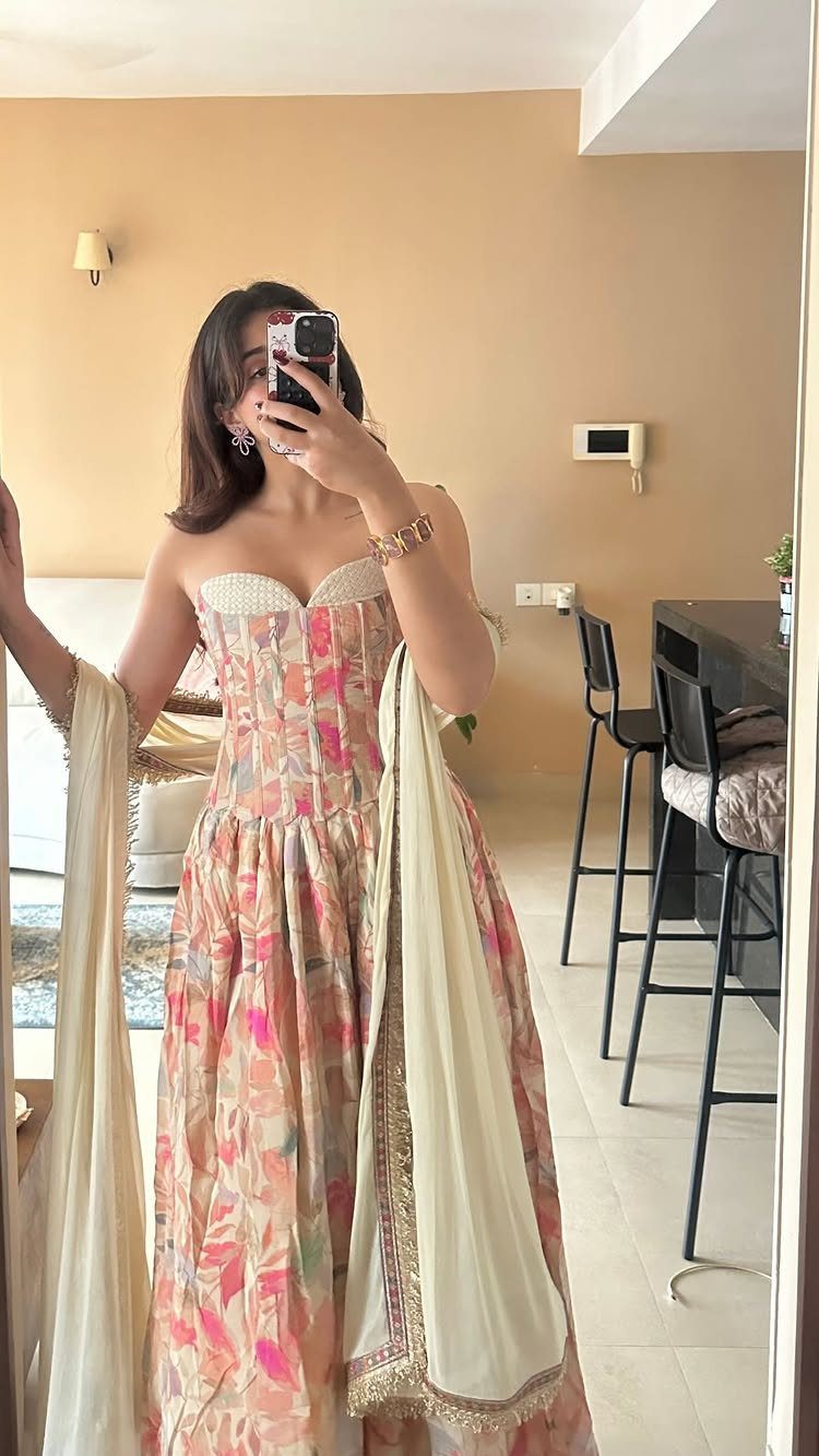 Woman in a floral corset gown and cream dupatta taking a mirror selfie.