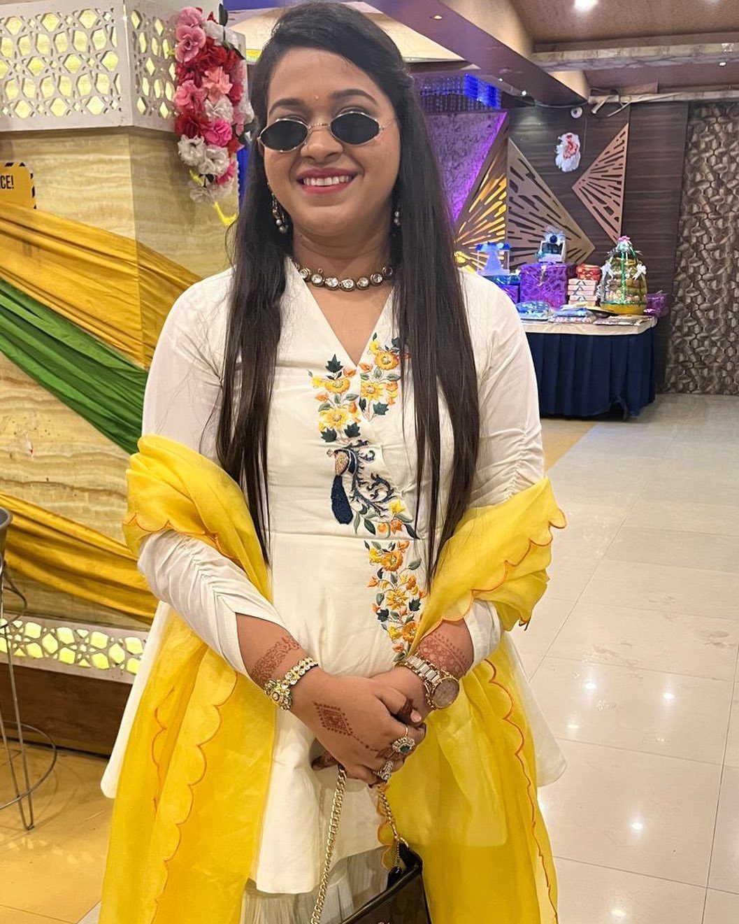Woman in ivory embroidered tunic and yellow dupatta posing in a decorated room.