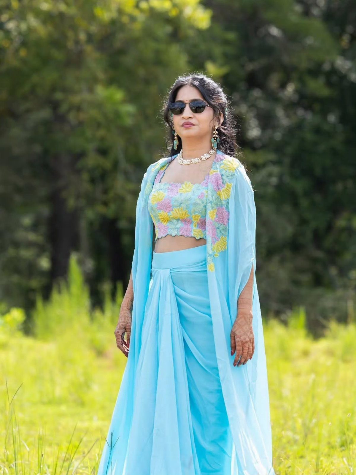 Woman in a light blue floral saree and cape posing in a green field