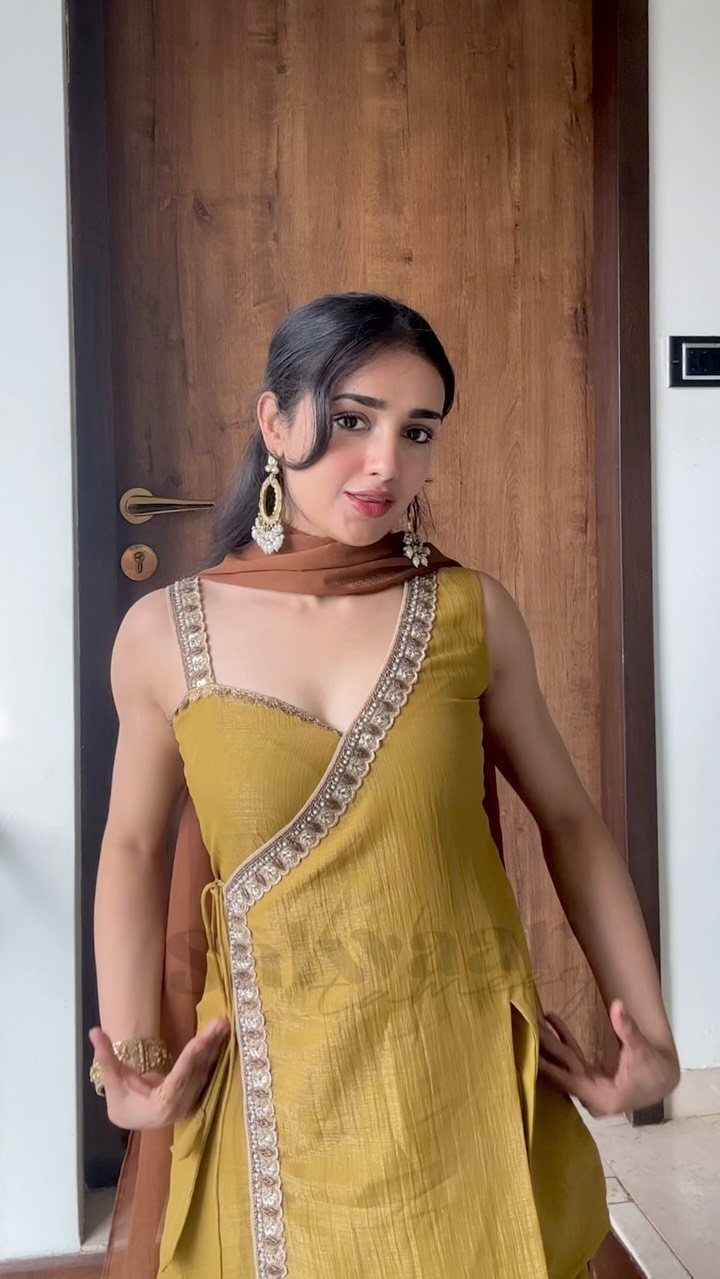 Woman in mustard yellow sleeveless suit set with silver embroidery and brown dupatta.
