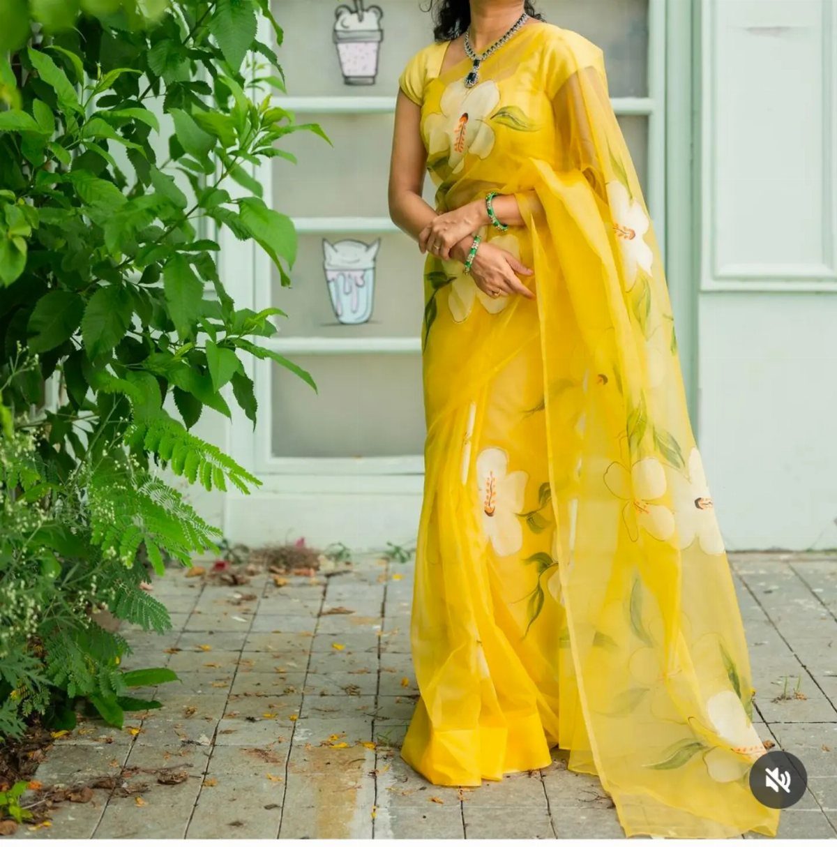 Woman in a yellow organza saree with white floral prints standing outdoors.