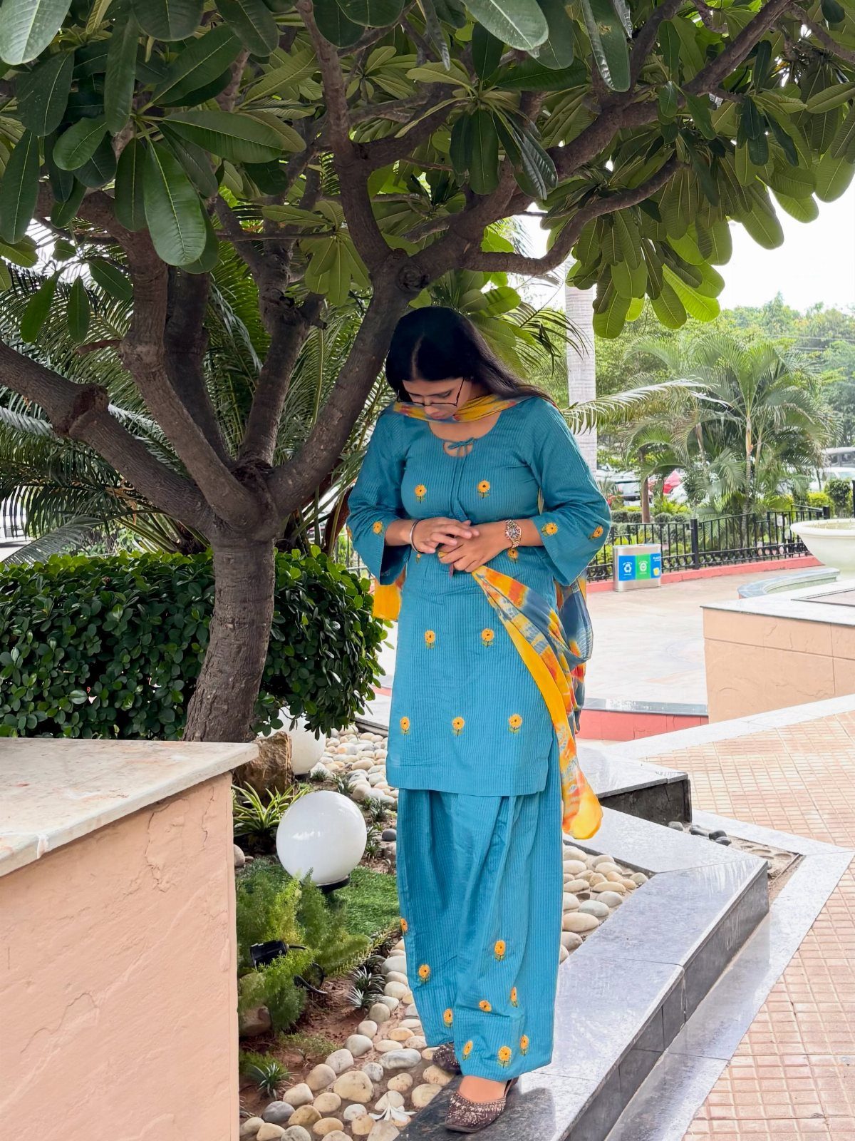 Woman in teal blue kurta and trouser set with yellow dupatta standing outdoors.