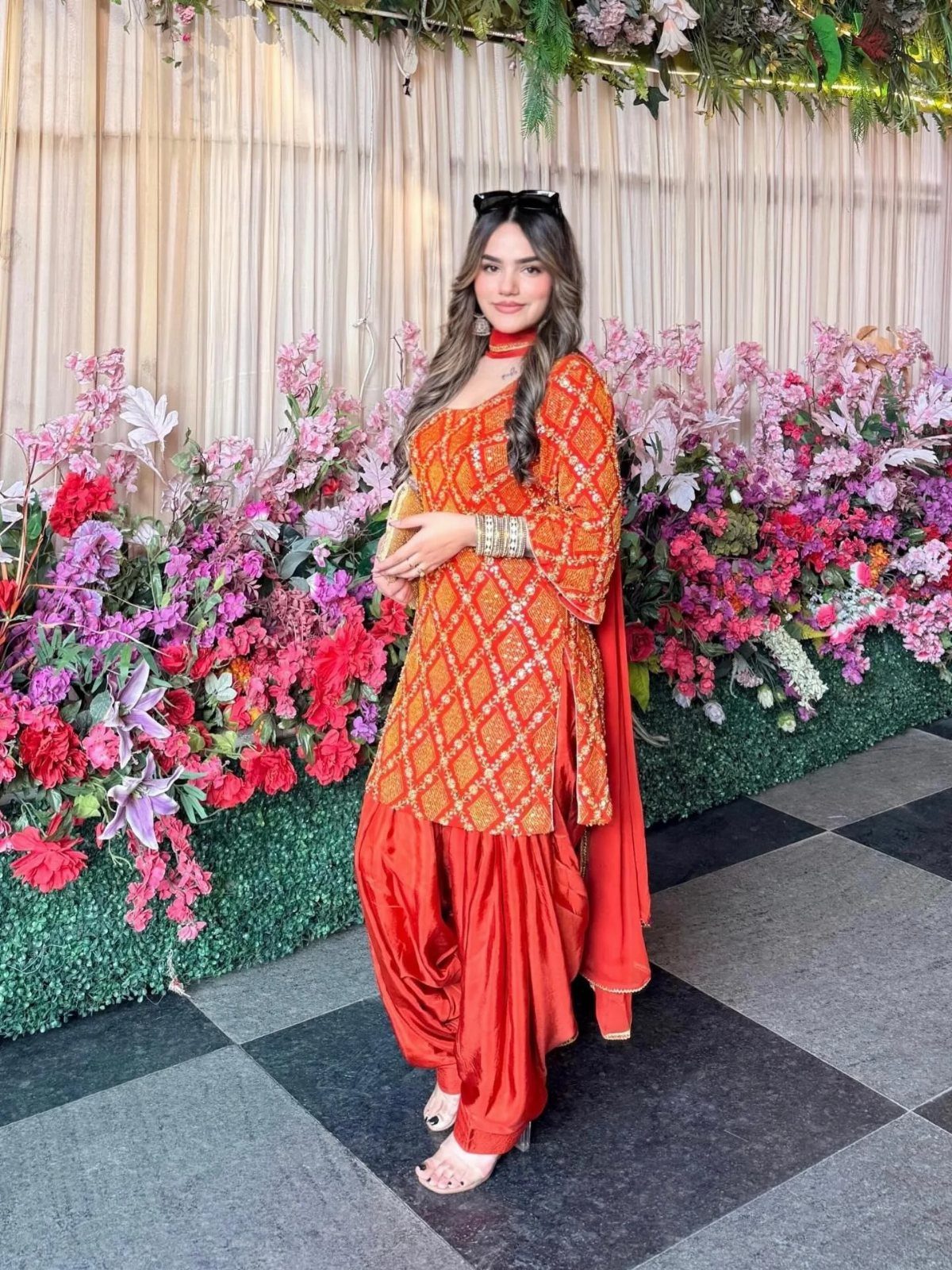 Woman wearing an orange Patiala suit with embroidered kurta and pleated salwar pants.