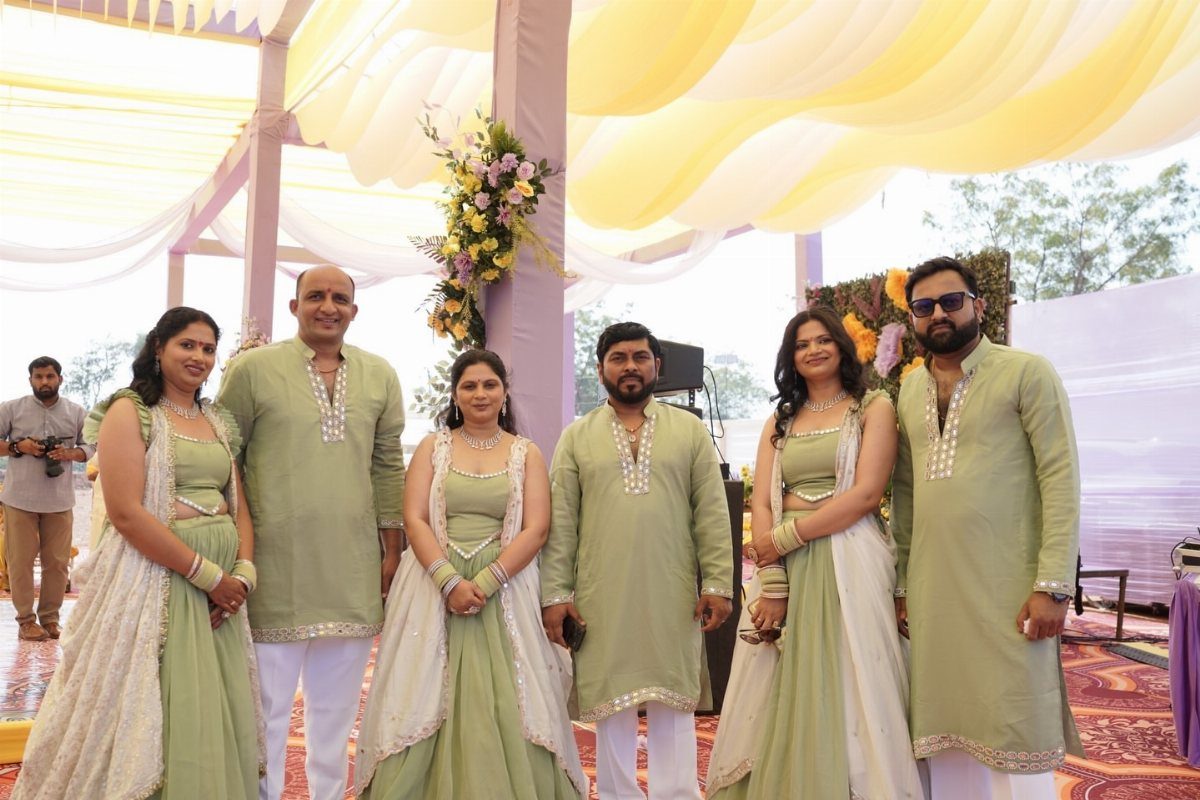 Group of people wearing coordinating pista green Indian lehengas and kurta sets outdoors.