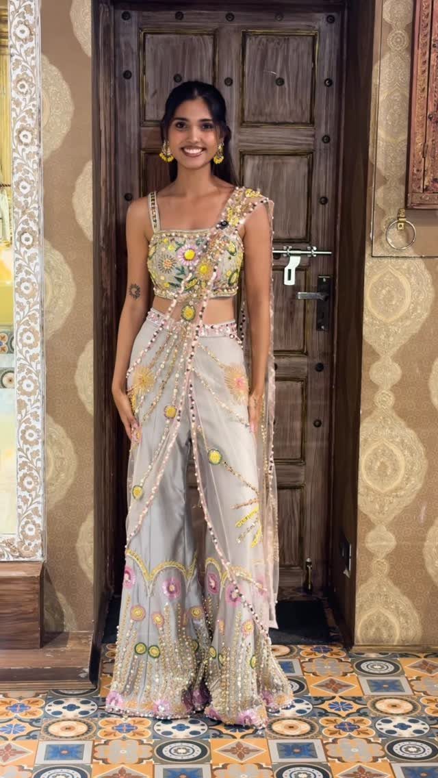 Woman wearing a light grey pre-draped saree with floral embroidery and mirror work.
