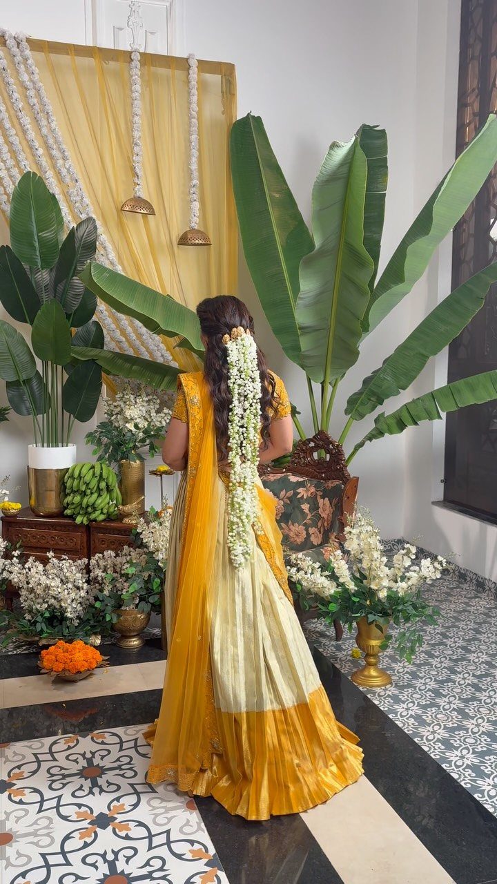 Woman from behind in a yellow tissue saree with floral hair adornments.