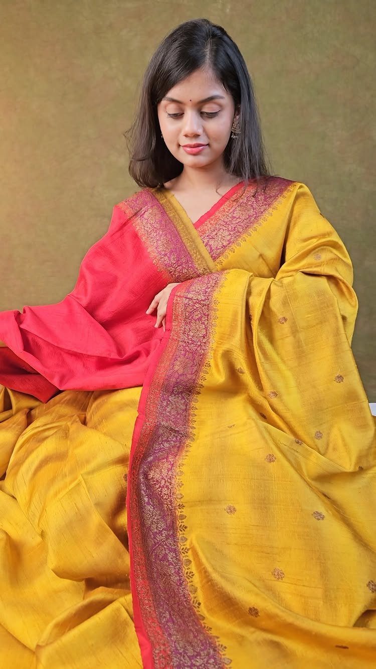 Woman wearing a yellow silk saree with a pink and gold zari border.