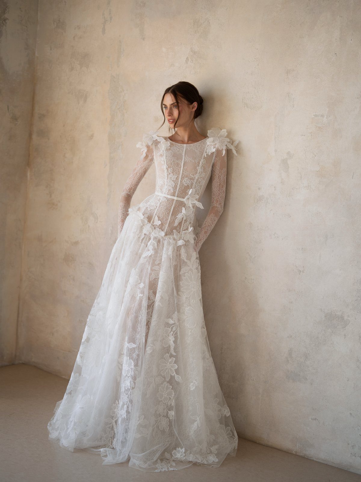 Woman in a white lace wedding gown with a sheer corset and long sleeves.