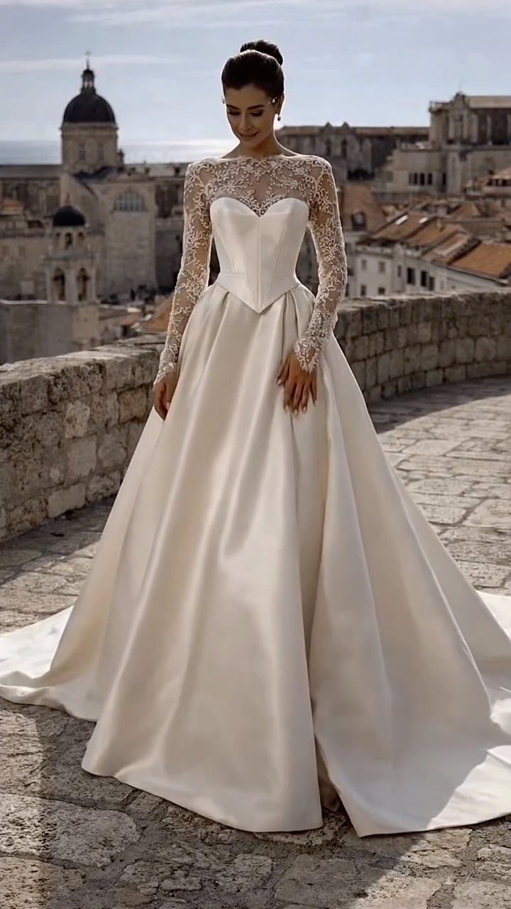 Woman in white satin wedding gown with pointed corset bodice and lace sleeves.