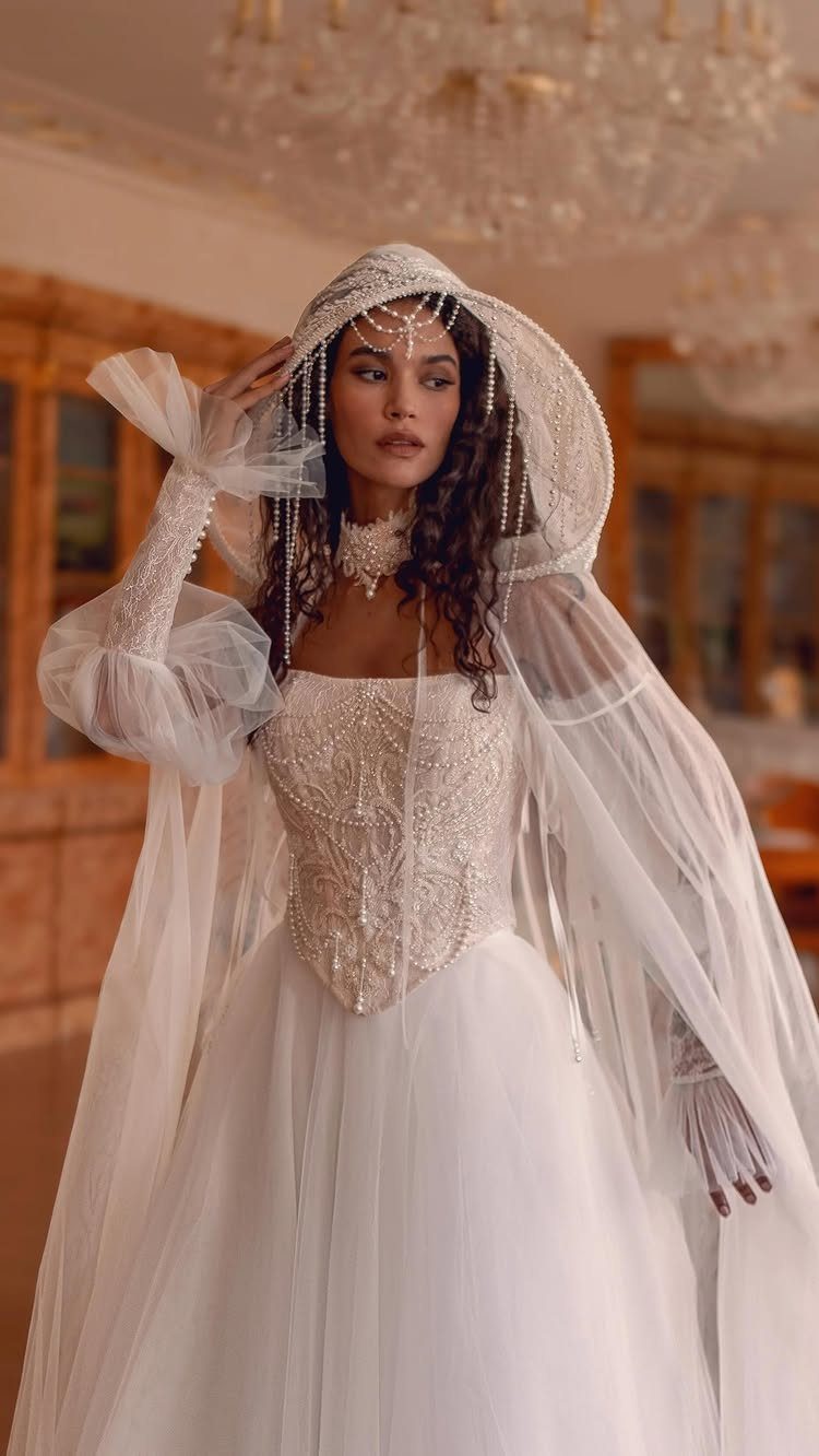 Woman in a white bridal gown with a pointed lace corset and pearl hood.