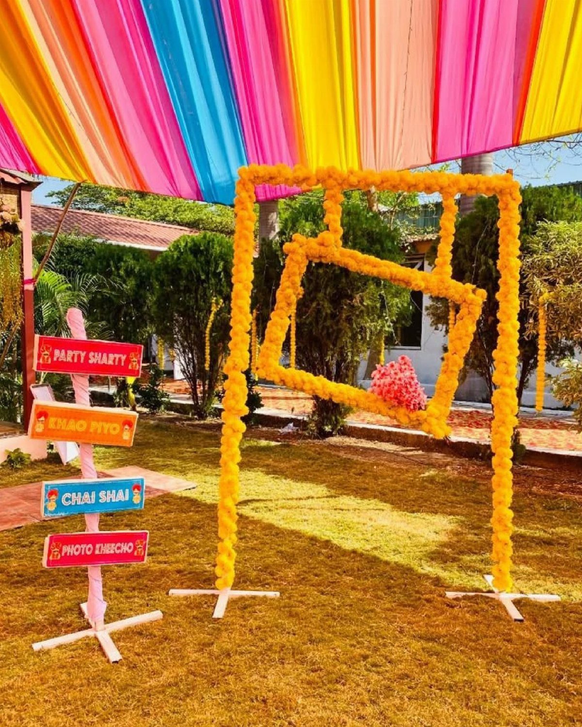 13 Mehndi Decoration Ideas for Outdoor Parties 6 Yellow floral frame and colorful fabric canopy at an outdoor mehndi event setup.