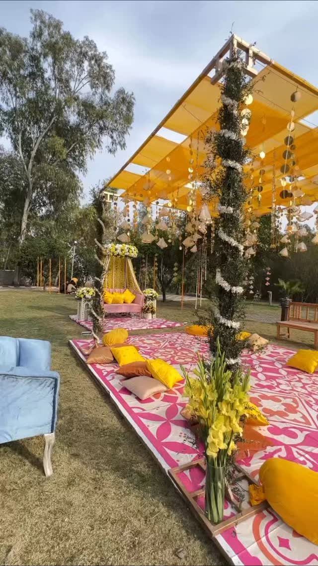 13 Mehndi Decoration Ideas for Outdoor Parties 5 Outdoor seating arrangement with yellow canopy, colorful floor cushions, and floral decorations on grass.