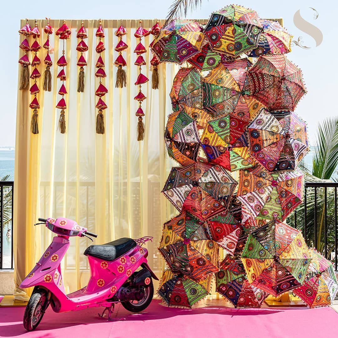 13 Mehndi Decoration Ideas for Outdoor Parties 13 Pink scooter and colorful umbrella wall decoration for an outdoor mehndi event.