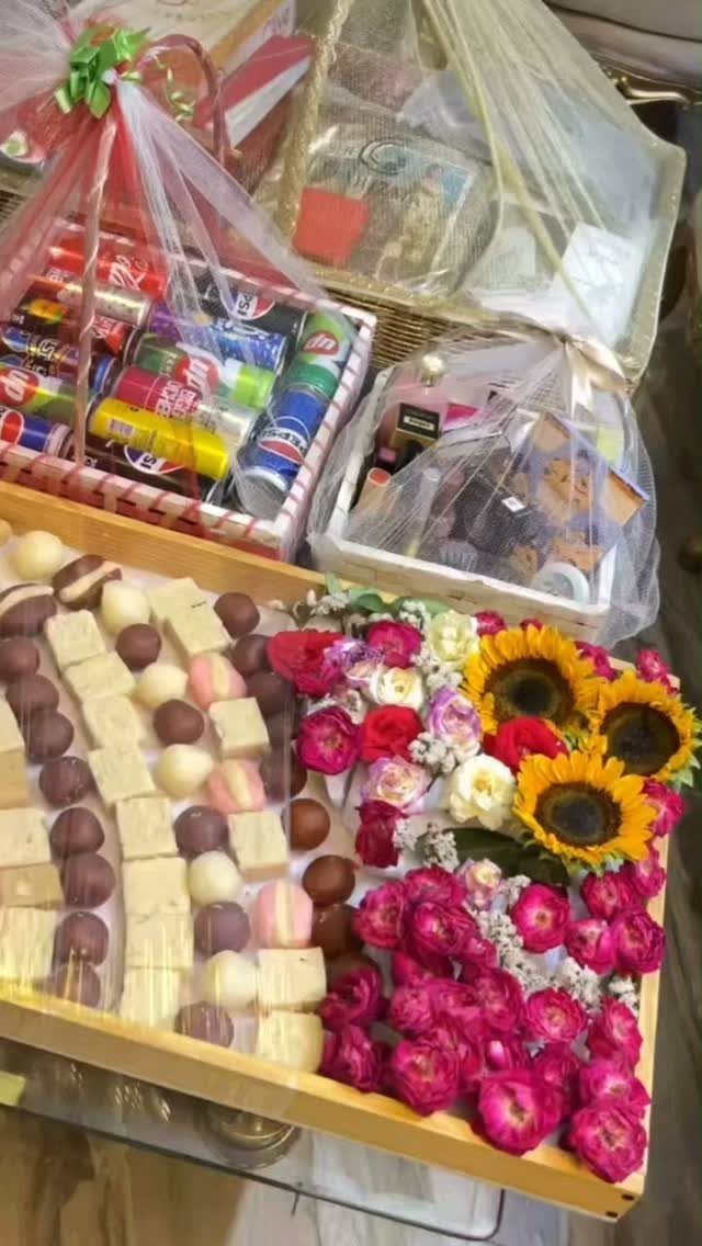 Gold tray of sweets and flowers with gift baskets of drinks in background