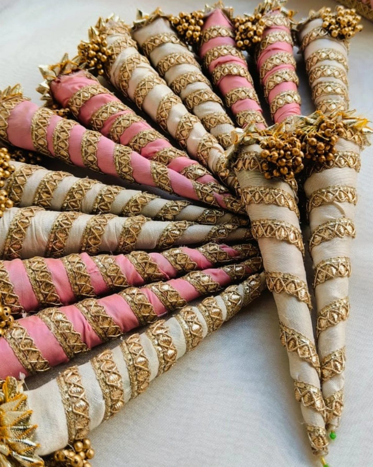 Pink and cream fabric mehndi cones decorated with spiraling gold gota lace ribbons.