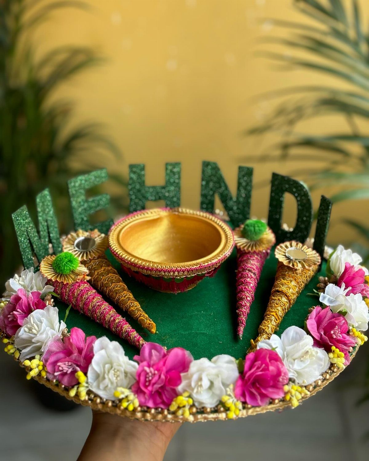 Green velvet mehndi tray with pink and white flowers, gold bowl, and henna cones.