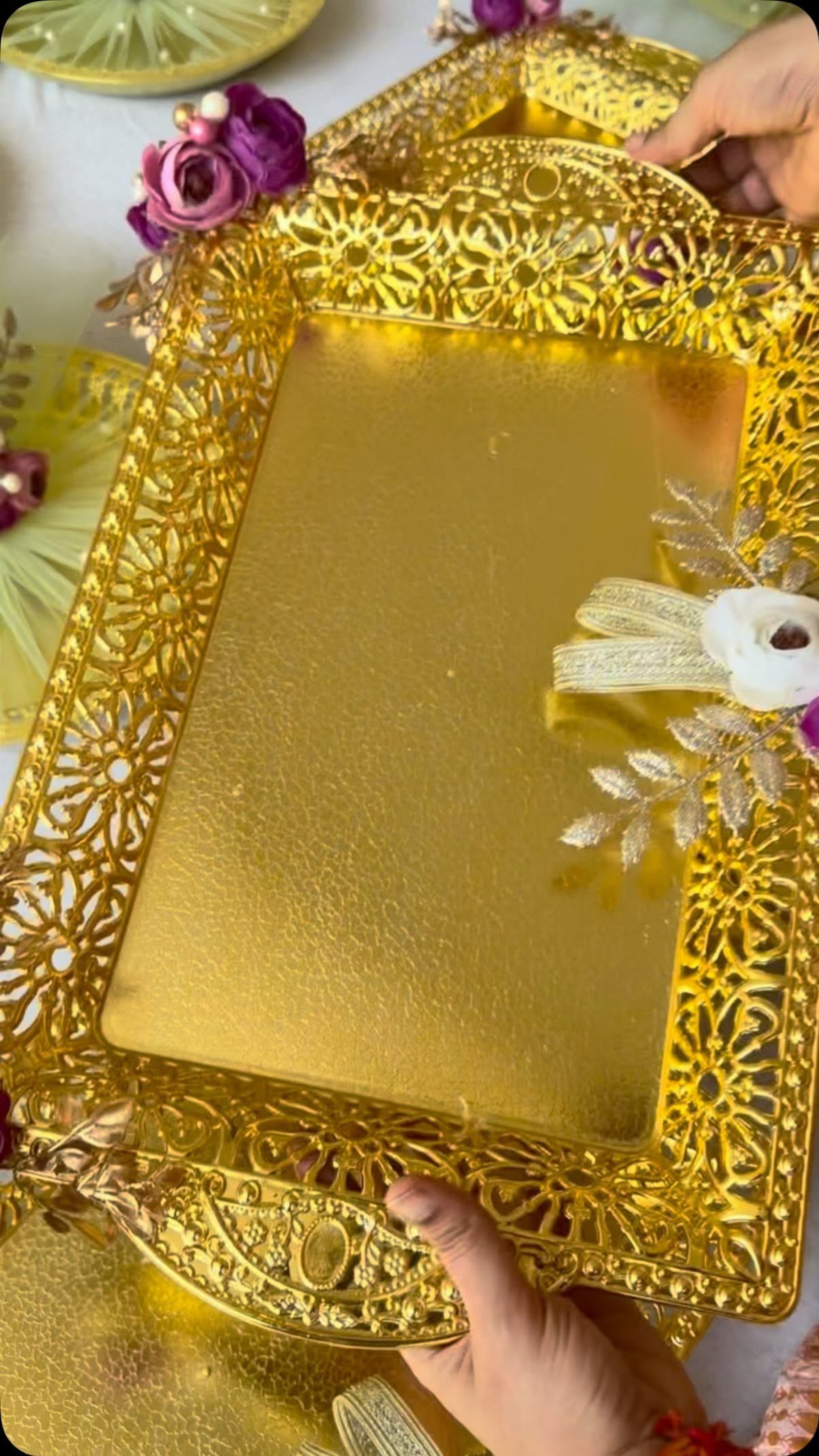 Gold filigree mirrored tray decorated with purple and white flowers held by hands.