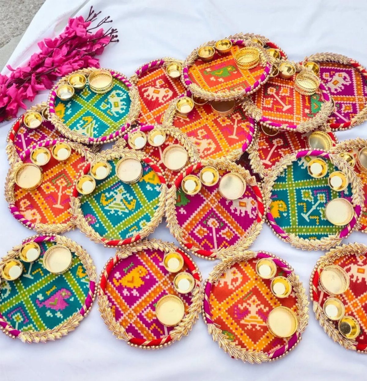Round Patola silk platters with gold braided borders and small gold bowls.