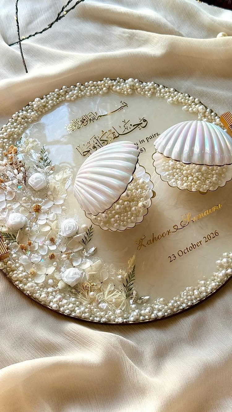 Pearl-beaded circular tray with shell bowls and white flowers on cream fabric.