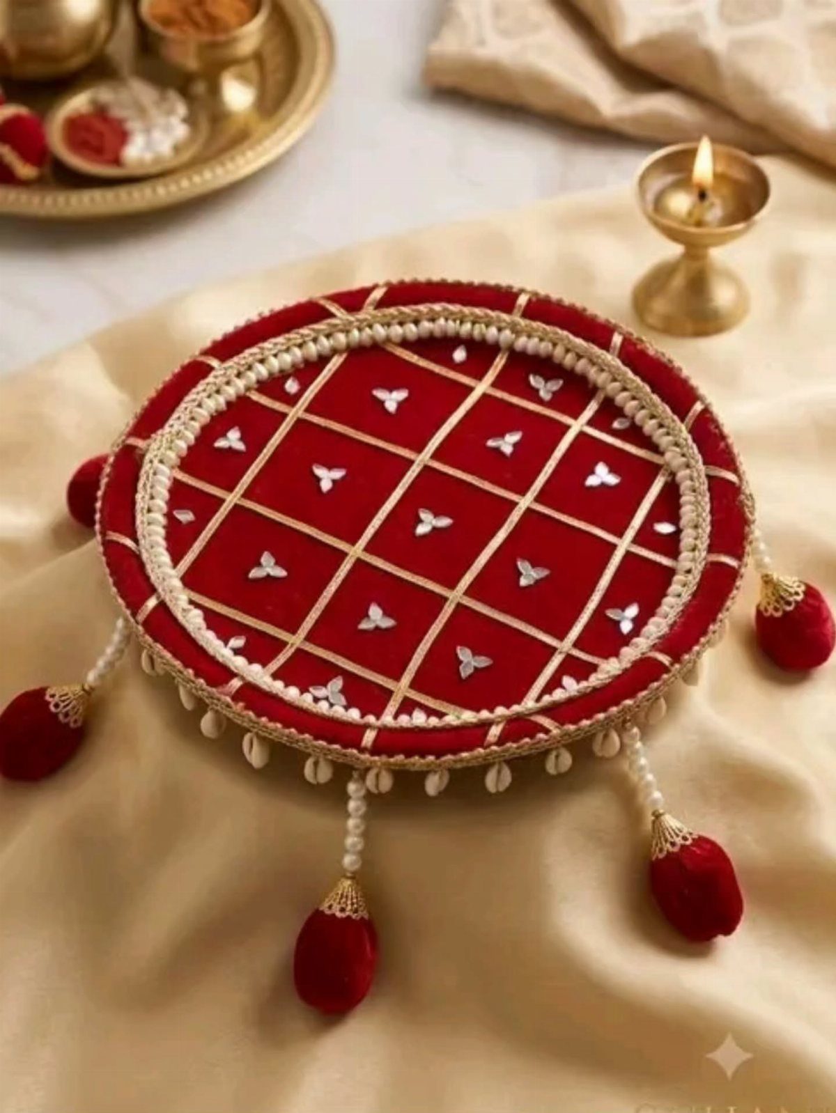 Red velvet circular tray with gold lattice and pearl decorations on cream fabric.