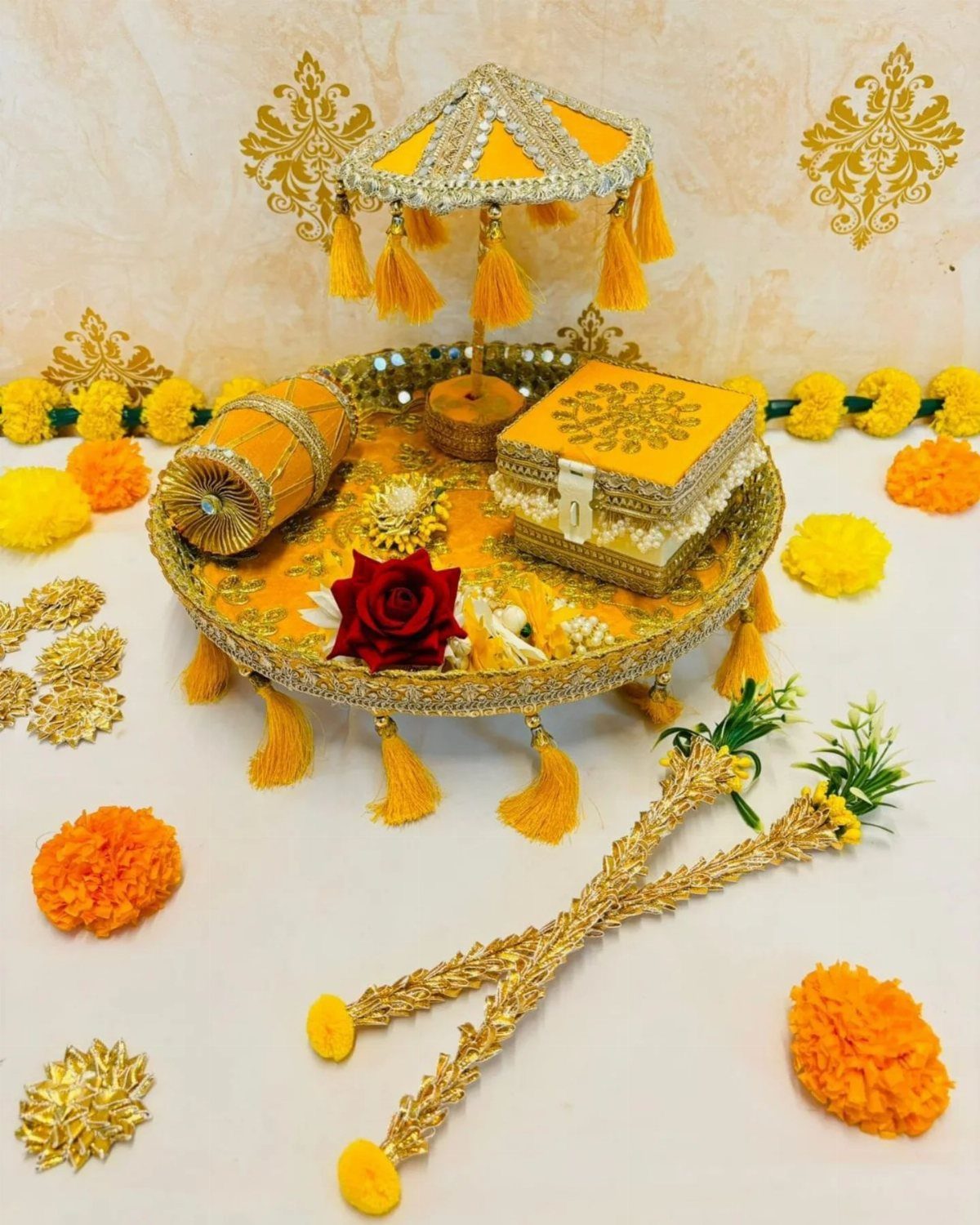 Decorative yellow mehndi platter with a small ornate umbrella, dhol, and red rose.