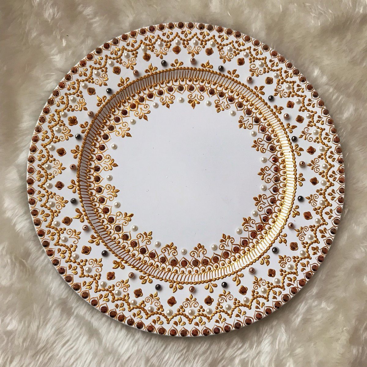 White circular platter with gold filigree patterns and pearls on white faux fur.