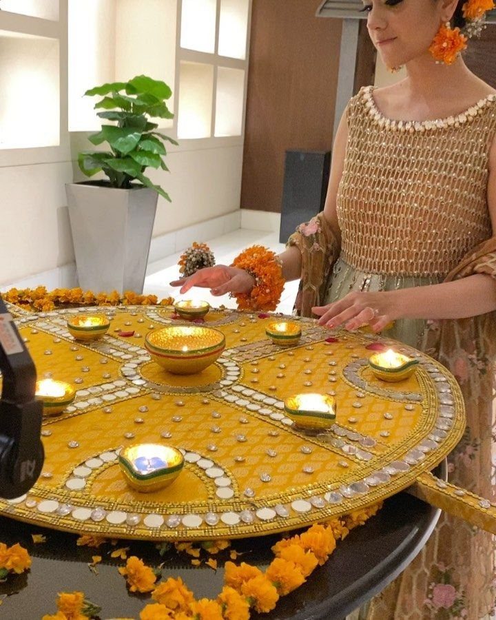 Yellow circular platter decorated with mirrors and diyas, surrounded by orange marigold flowers.