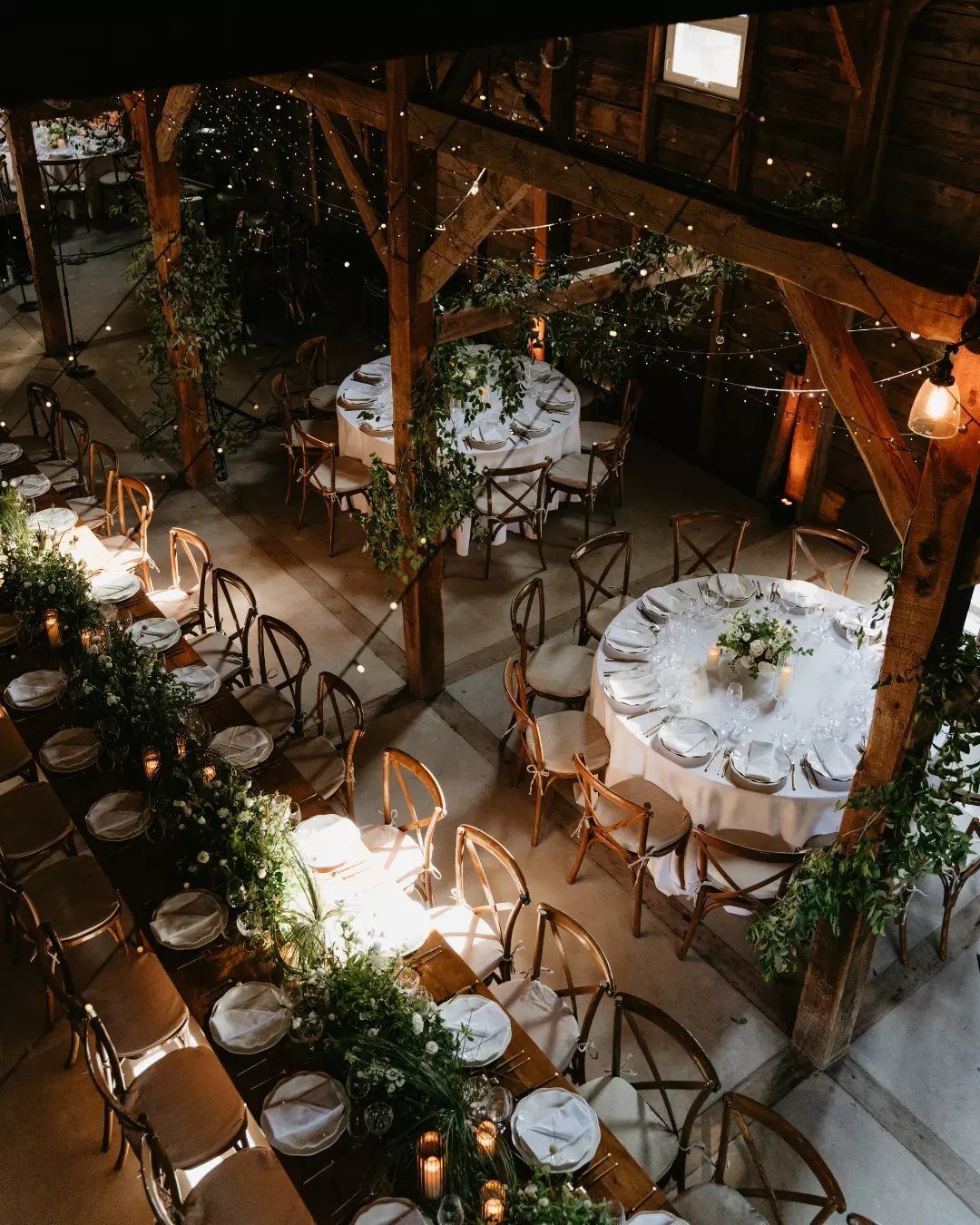 Rustic barn interior with decorated wedding tables, white linens, and warm string lighting.
