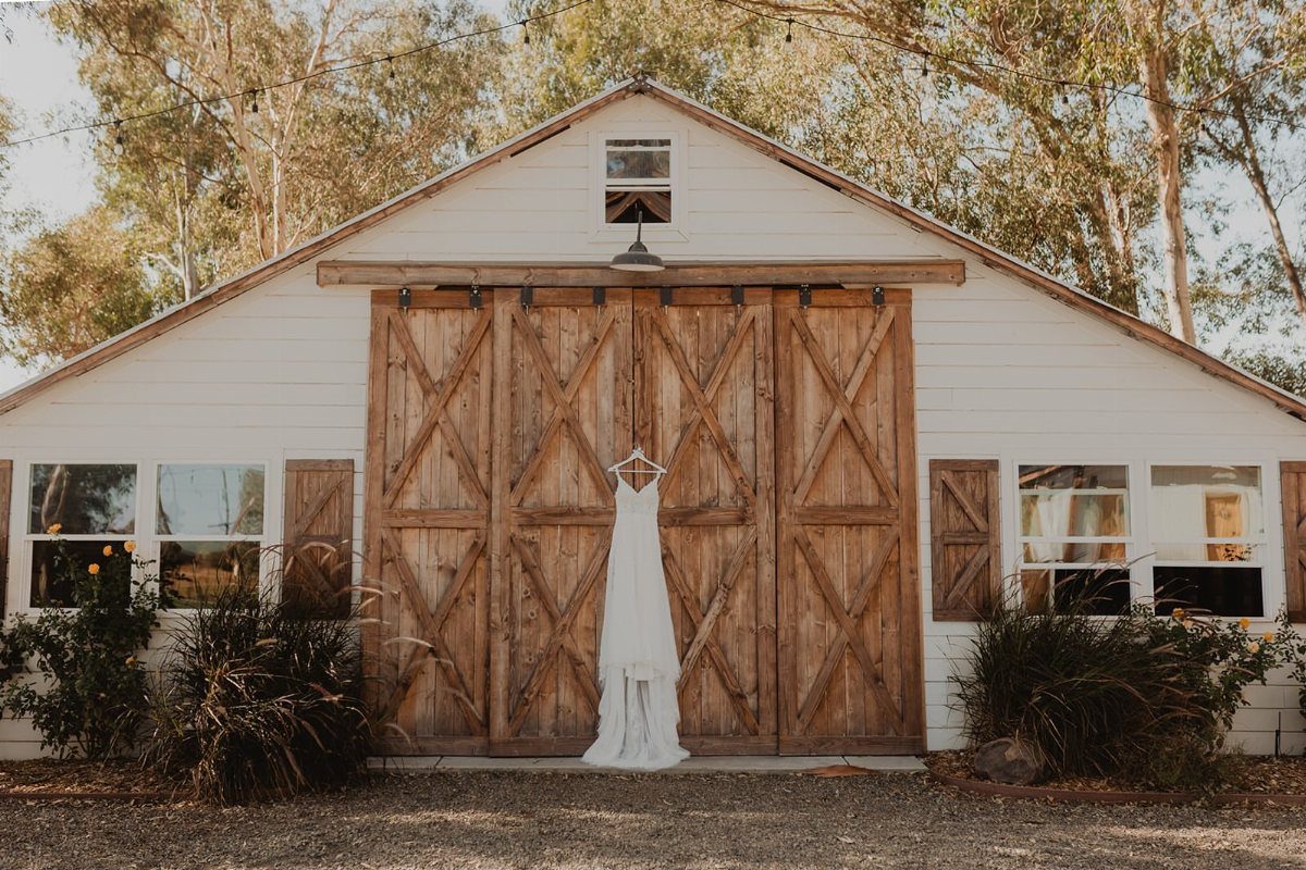 White wedding dress hanging on wooden barn doors of a modern white venue