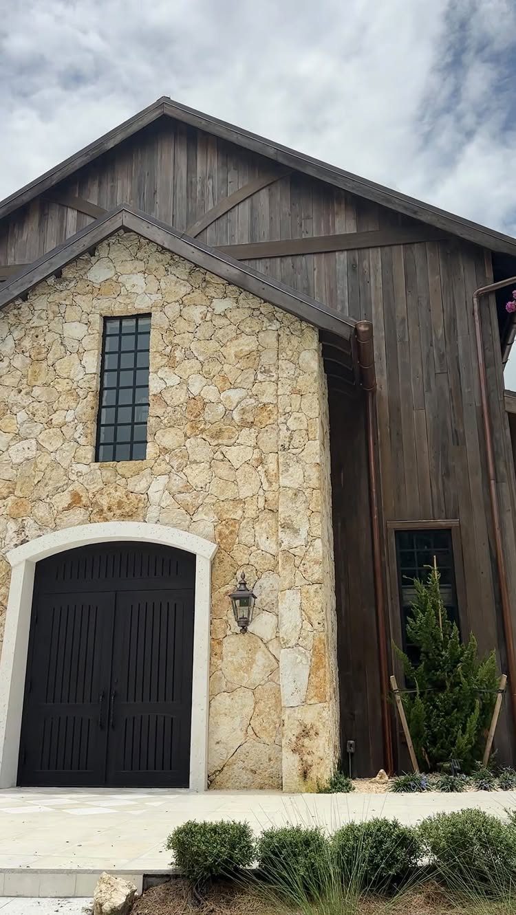 Modern barn with light stone walls, dark wood siding, and black arched doors.