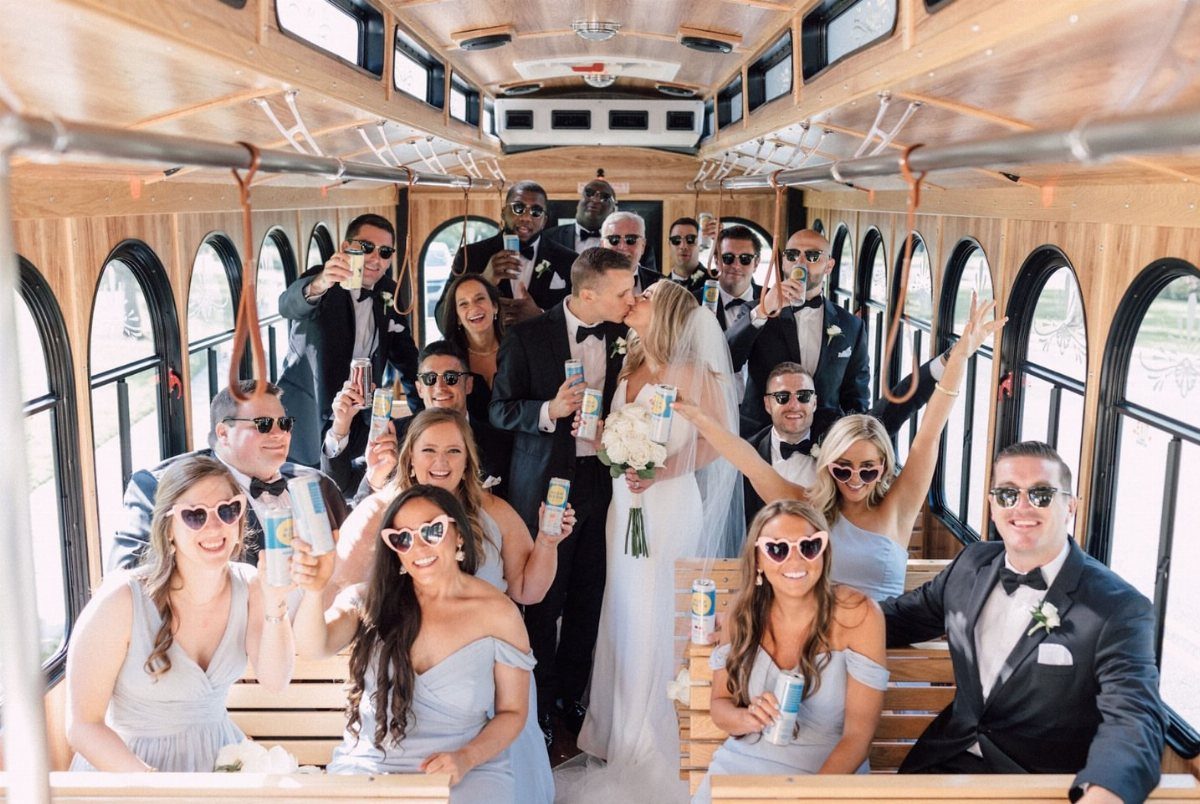 Wedding party and couple celebrating inside a wooden trolley shuttle bus.